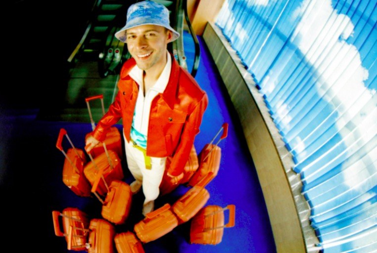 A man in an orange jacket surrounded by orange suitcases